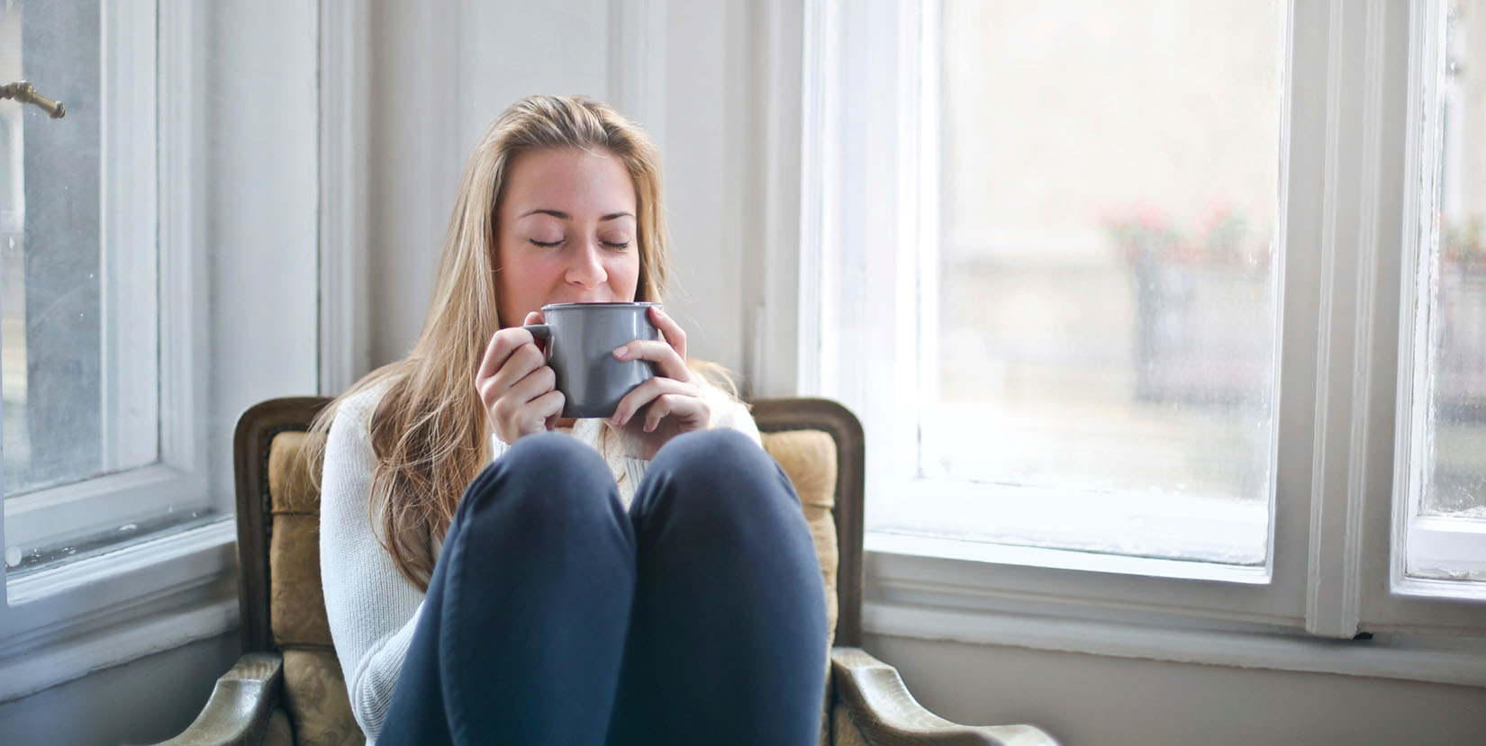 Woman sitting, holding cup - Many of us now have more time to sit and ruminate in our anxiety - how can we stay present and keep ourselves less stressed during this time?