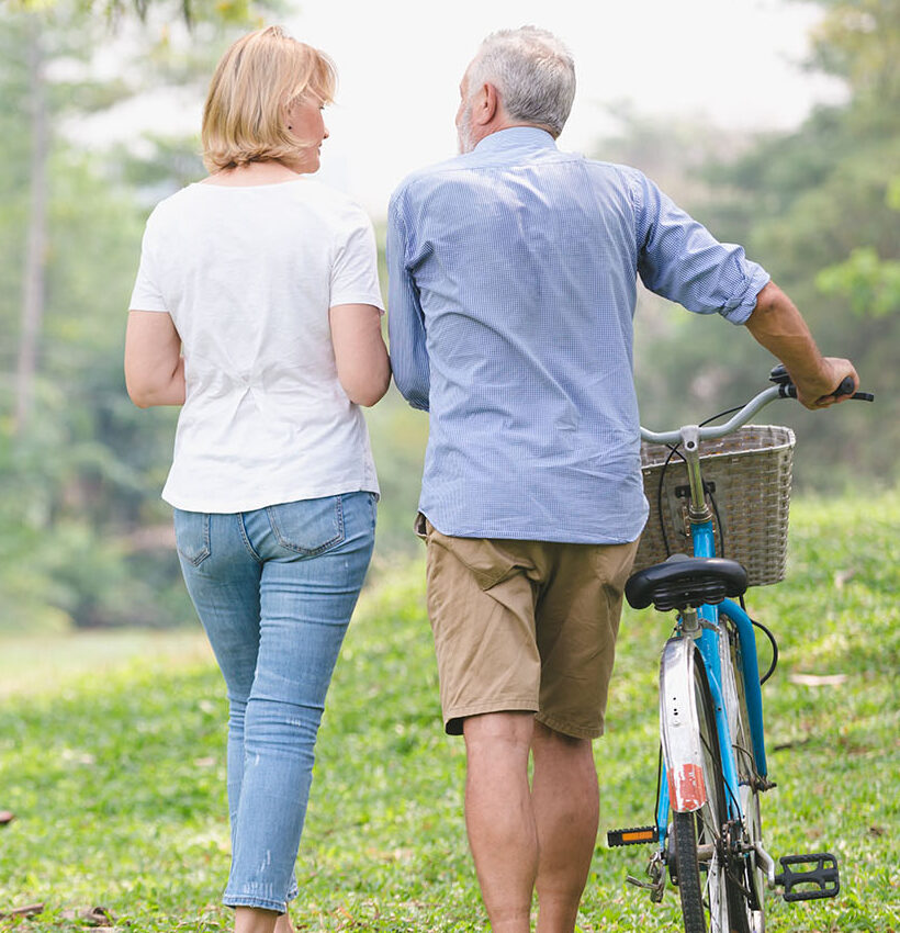 Senior couple walking their bike Active seniors like these two walking and riding their bikes need chiropractic care for seniors to stay active and free from pain.